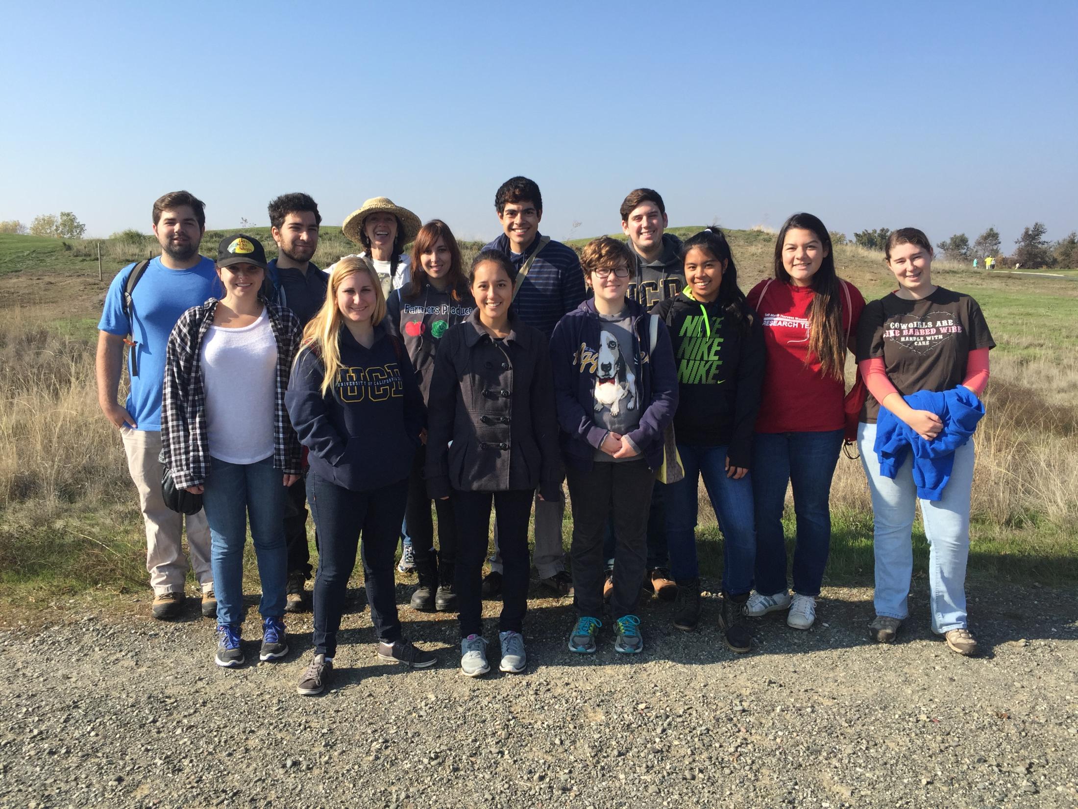 A group of thirteen smiling men and women in a field